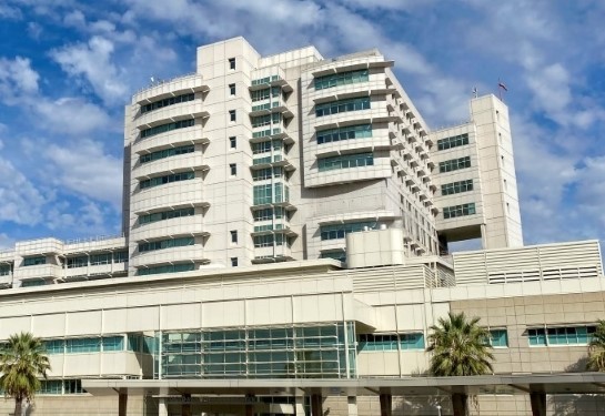 Exterior of UC Davis Medical Center with multi-story hospital buildings under a blue sky with scattered clouds.